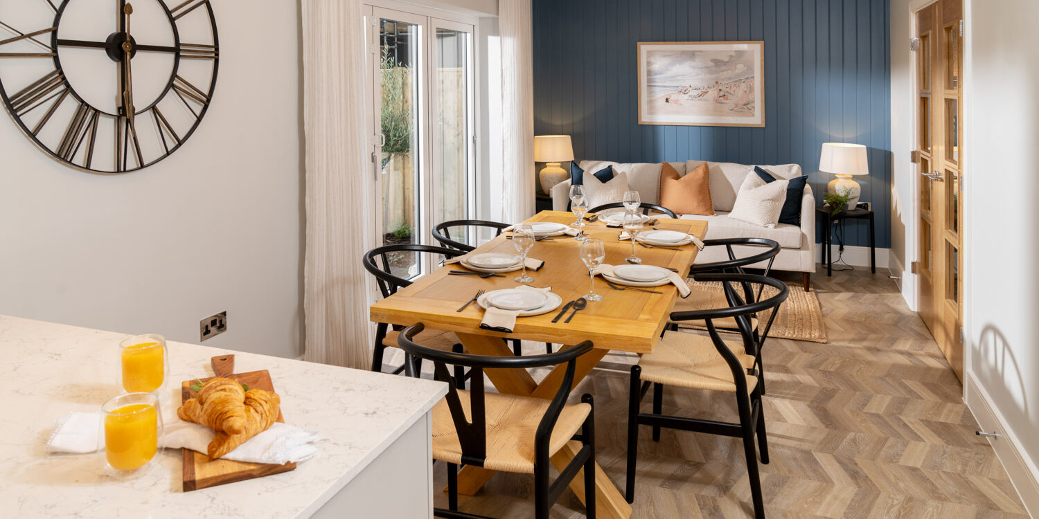 Open plan dining area with dining table and chairs at the middle with dark blue far wall and cream sofa to the rear