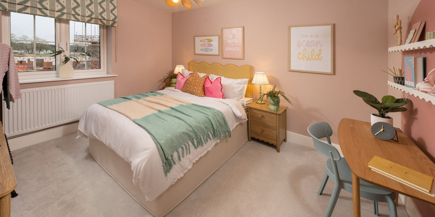 Pink and green pastel coloured bedroom with bedside table with lamp and made up bed. window to the rear