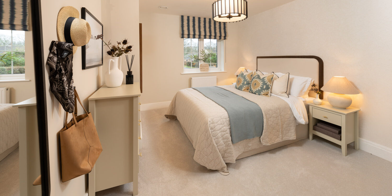 cream and blue bedroom with chest of drawers to the foot of the made up bed and window to the rear